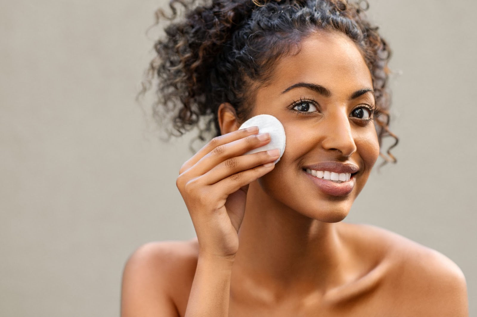 Young pretty african american woman taking off makeup with cotton wipe sponge