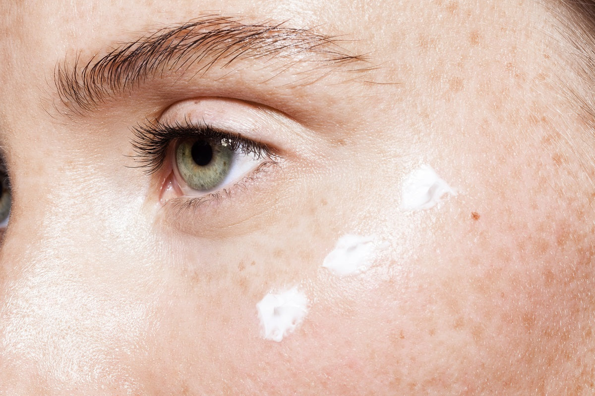 Close up of beautiful woman face with clean fresh skin and points of white moisturizing cream under eye
